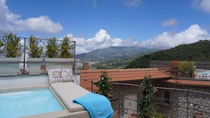 Area piscina sul tetto con una poltrona da relax e un asciugamano blu, con vista su un paesaggio montuoso.