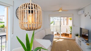 Un soggiorno moderno con un lampadario in vimini, un divano, una televisione e vista sull'esterno.