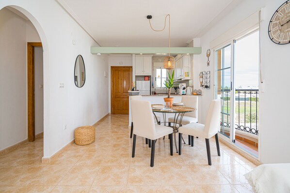 A modern kitchen with white cabinets, a dining area with a glass table and white chairs, and a large window with a view of the outdoors.