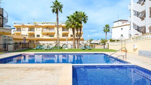 Una piscina con bordo piastrellato, circondata da palme e un edificio a più piani con balconi.