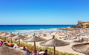 A beach with thatched umbrellas, a poolside area, and a building with a Mediterranean architectural style.