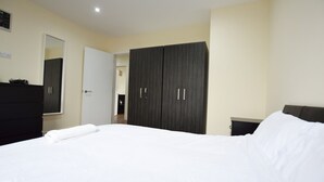 A bedroom with a large bed, a dark wardrobe, a dresser, and a mirror on the wall. - 1-bed Apartment in Ealing, 3 Mins From Station (London)