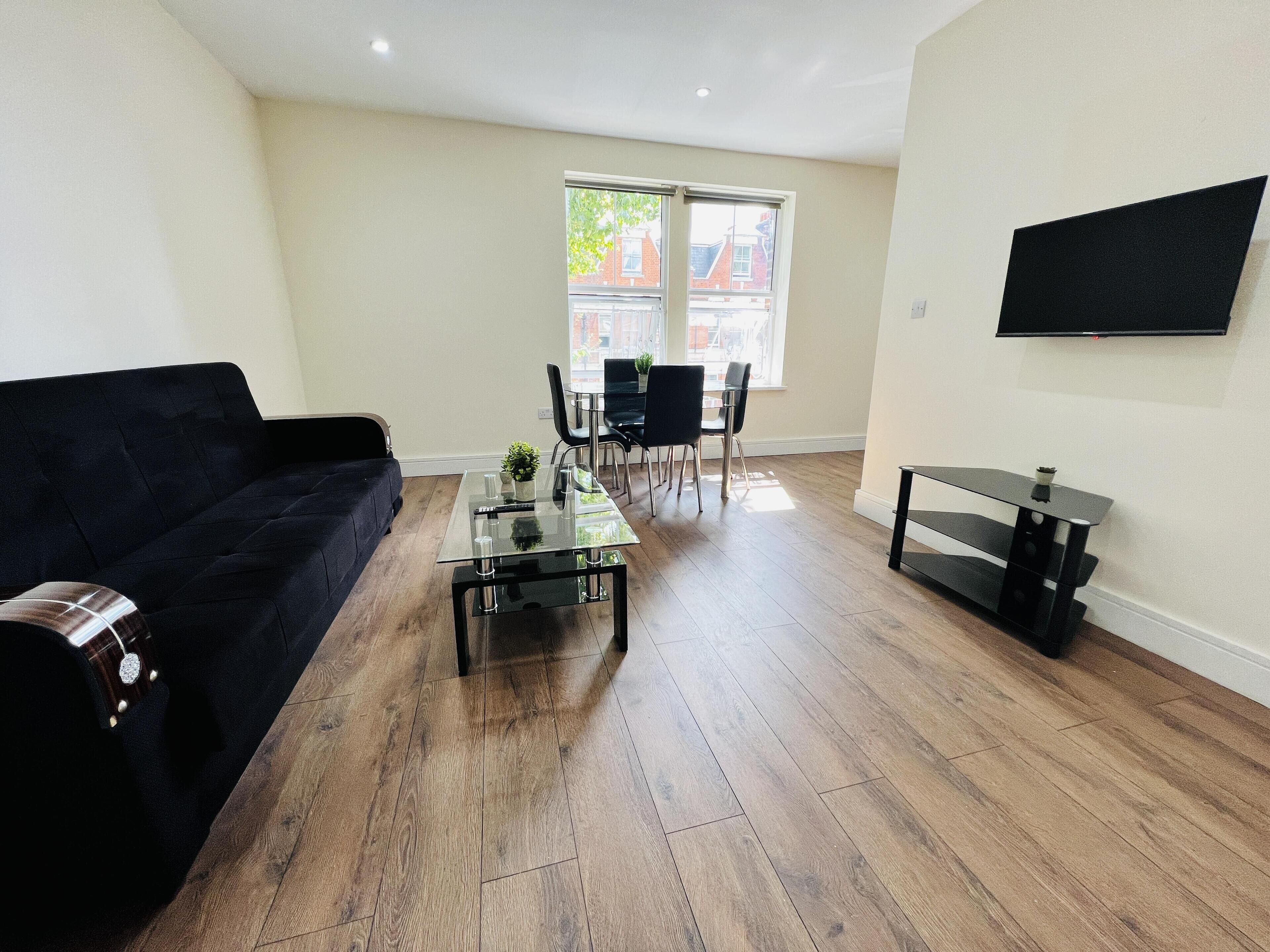 A modern living room with a dark sofa, a glass coffee table, and a dining area with chairs and a table.