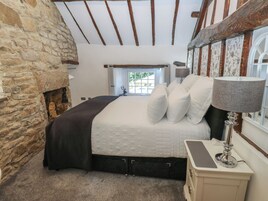 Un dormitorio con pared de piedra, cama con ropa blanca, lámpara y ventana con vistas.