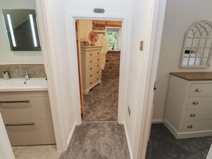 Un corridoio stretto con pavimento rivestito di moquette, una porta bianca che conduce a una stanza con parete in pietra, uno scaffale in legno e uno specchio appeso al muro.
