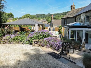 A garden with a patio area, stone walls, and a conservatory.