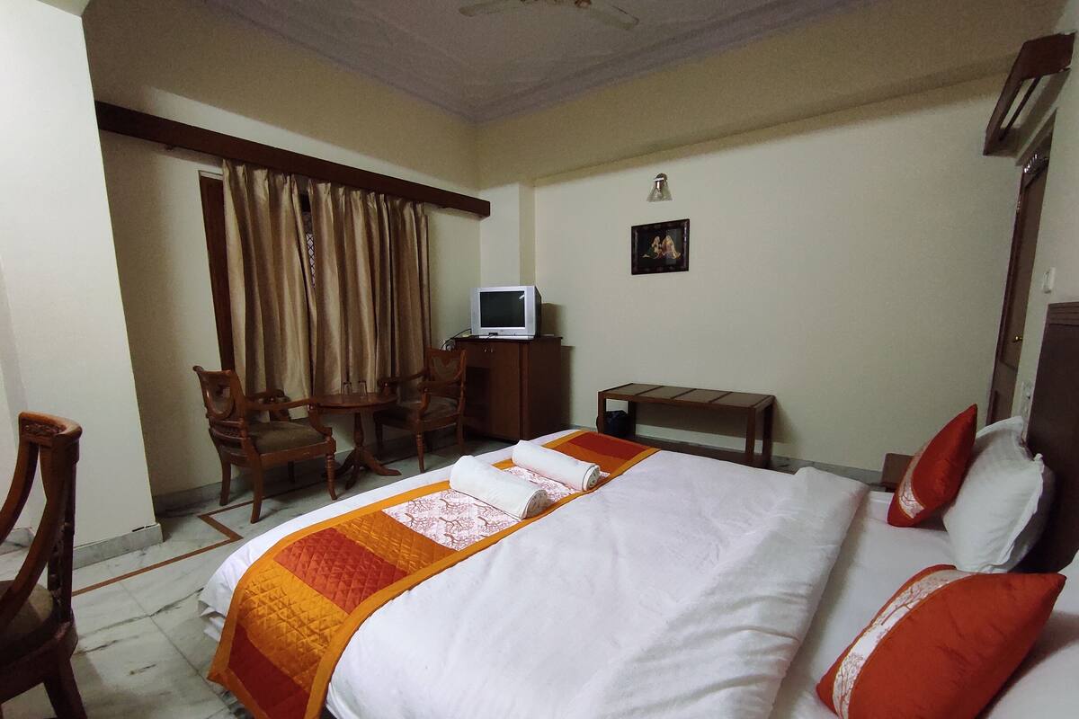 A hotel room with a bed, a desk, a chair, a television, and a small table.