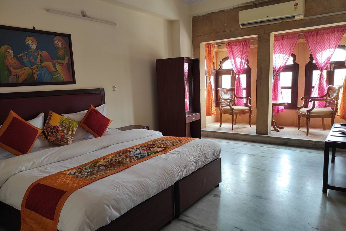 A hotel room with a large bed, a wardrobe, a desk, and a view of the outside through a window with curtains.