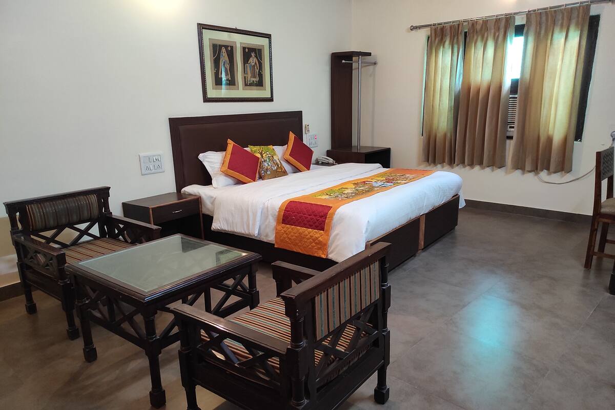 A hotel room with a bed, a glass-top table, two wooden chairs, a nightstand, and a wall-mounted telephone.