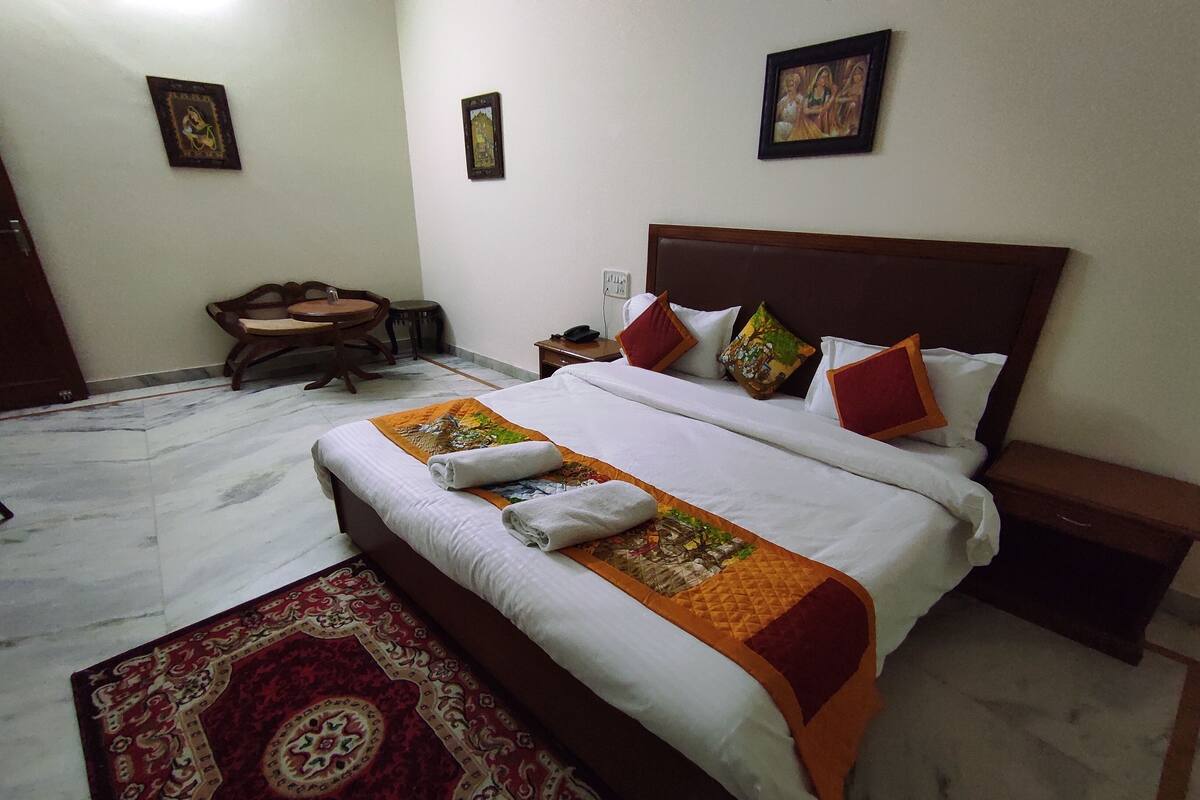 A neatly made bed with a white and orange bedspread, a red and gold patterned rug, and a wooden headboard.