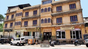 A multi-story building with a ground floor that appears to house a hotel named "Hotel Sohandeep." There are several shops on the ground floor, including one with a sign for "Rajasthan Handloom & Handicrafts." The building has a traditional architectural style with multiple windows on each floor. - Hotel Sohandeep (Jaisalmer)
