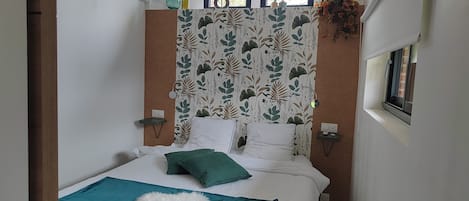 A narrow room with a bed, a small bedside table, and a window.