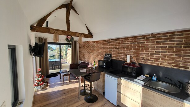 A kitchen with a brick wall, wooden beams, a dining area with a Christmas tree, and a sliding glass door leading to a patio.