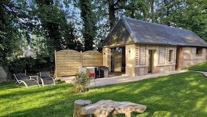 A rustic cabin with a stone bench and lounge chairs in a well-maintained garden.