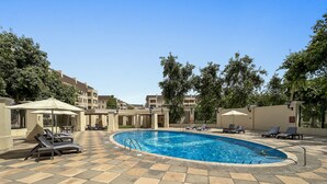 A swimming pool with lounge chairs and umbrellas, surrounded by a tiled patio and trees. - Elegant Apartment Retreat at Widcombe House 3 (Dubai)