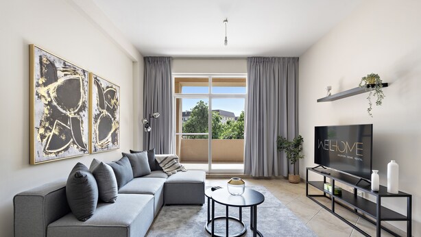 A modern living room with a grey sofa, a coffee table, a TV on a black stand, and a large window with curtains. - Elegant Apartment Retreat at Widcombe House 3 (Dubai)