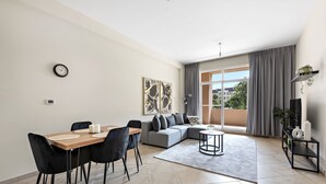 A modern living room with a dining area, grey sofa, and a large window with curtains. - Elegant Apartment Retreat at Widcombe House 3 (Dubai)