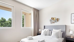 A modern hotel room with a large bed, two bedside tables, a window with curtains, and a decorative wall piece. - Elegant Apartment Retreat at Widcombe House 3 (Dubai)