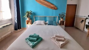 A bedroom with a large bed, two nightstands, a surfboard wall decoration, and potted plants. - Bologna Homestay (Bologna)