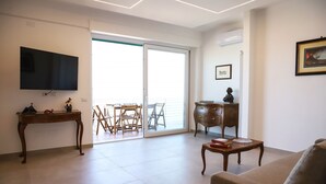 Un salon équipé d’un téléviseur à écran plat, d’une table basse en bois, d’un canapé, d’une table d’appoint en bois, d’une commode et d’un balcon avec une porte vitrée.