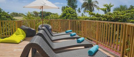 A wooden deck with lounge chairs and a yellow bean bag chair, surrounded by a wooden fence and lush greenery.