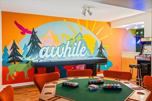 A room with a pool table, chairs, and a mural with the word "auhile" and a mountain scene.