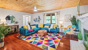 Una sala de estar acogedora con techo de madera, alfombra geométrica colorida y sofá azul con cojines amarillos.