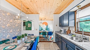 Una cocina moderna con techo de madera, armarios azules y un comedor con mesa dispuesta para cuatro.