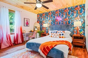 A bedroom with a wooden ceiling, a bed with a colorful headboard, a desk, and a chair.