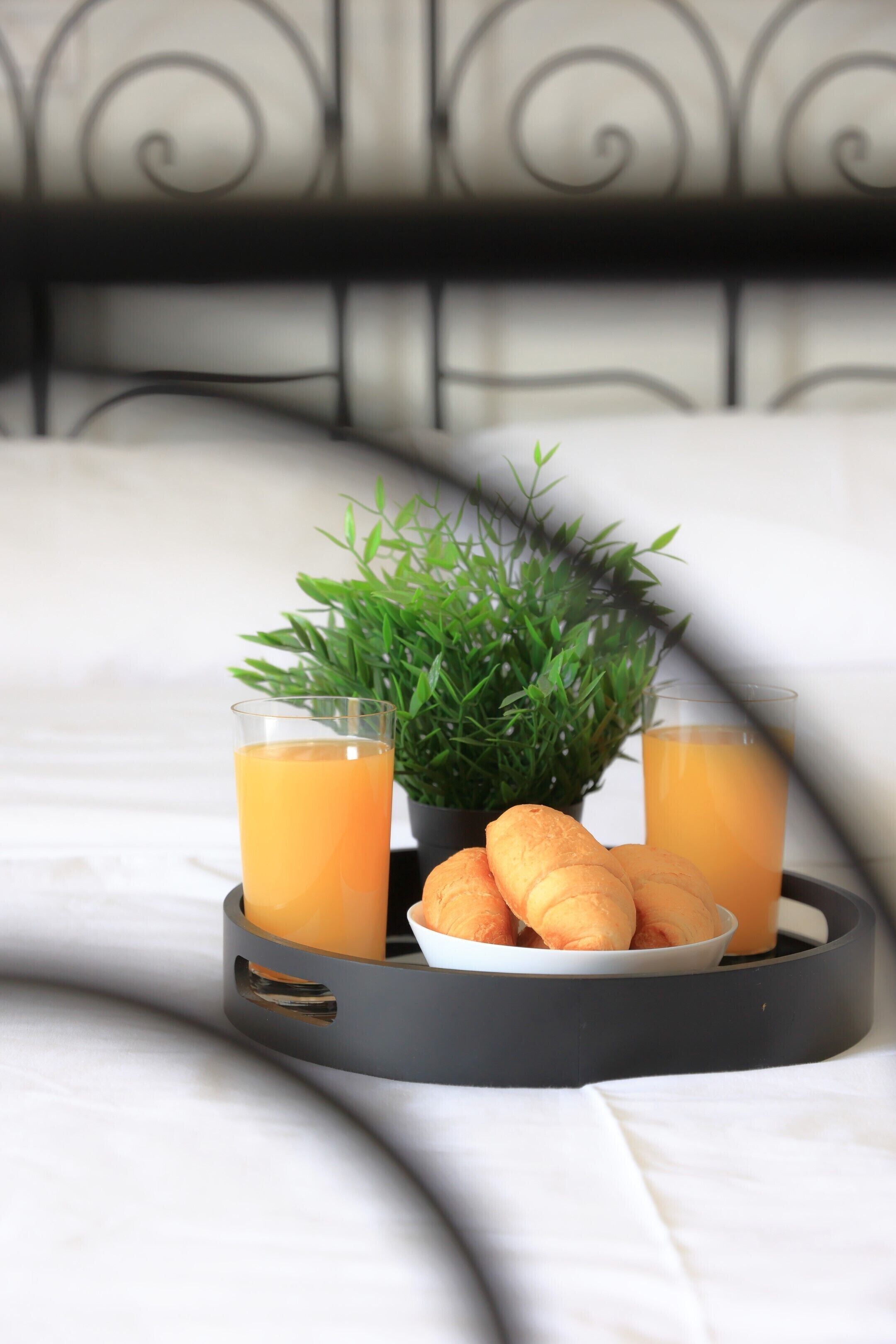 Un plateau avec deux verres de jus d’orange, un bol de croissants et une petite plante en pot, le tout posé sur une table recouverte d’une nappe blanche.