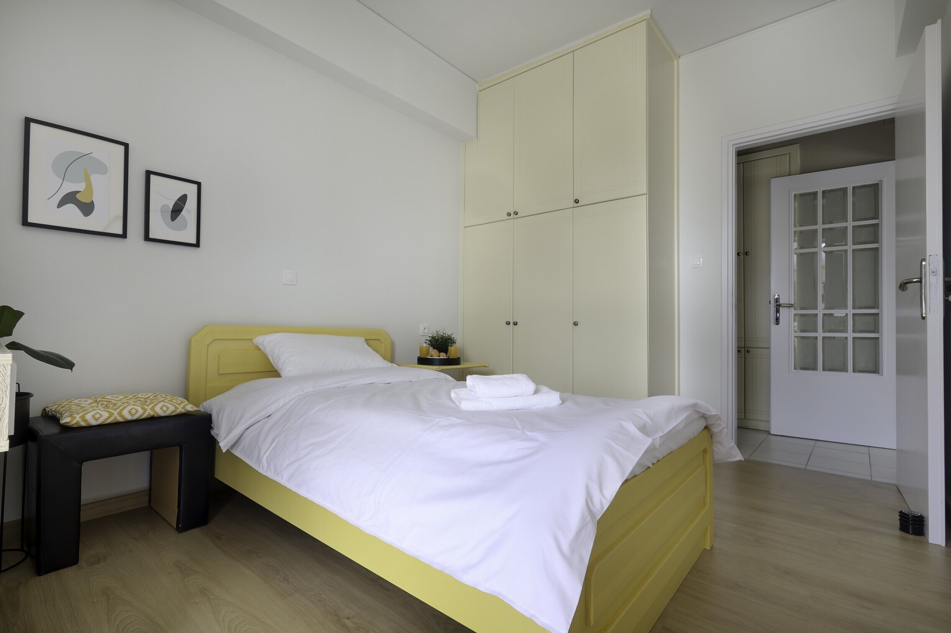 A bedroom with a bed, a bedside table, a small stool, a wardrobe, and a door.