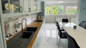 A modern kitchen with a marble countertop, stainless steel sink, and a dining area with a white table and black chairs. - Apartament Irun (Irun)
