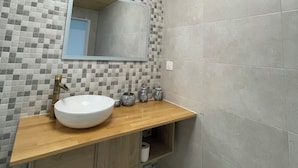 A bathroom with a wooden vanity, a white sink, a mirror, and a tiled backsplash. - Apartament Irun (Irun)