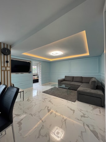 A modern living room with a sectional sofa, a glass coffee table, and a marble floor.