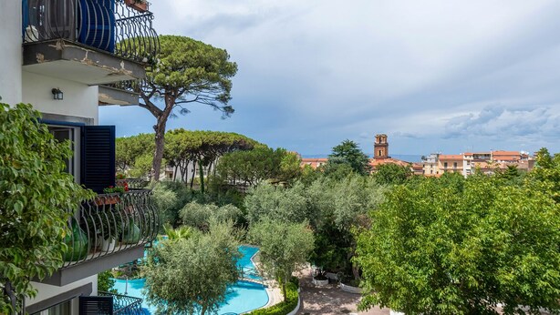 A residential building with a swimming pool, surrounded by trees and a view of a distant church tower. - Casa Bellis (Sorrento)