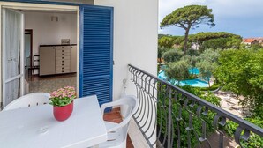A balcony with a table and chairs, a potted plant, and a view of a swimming pool and trees. - Casa Bellis (Sorrento)