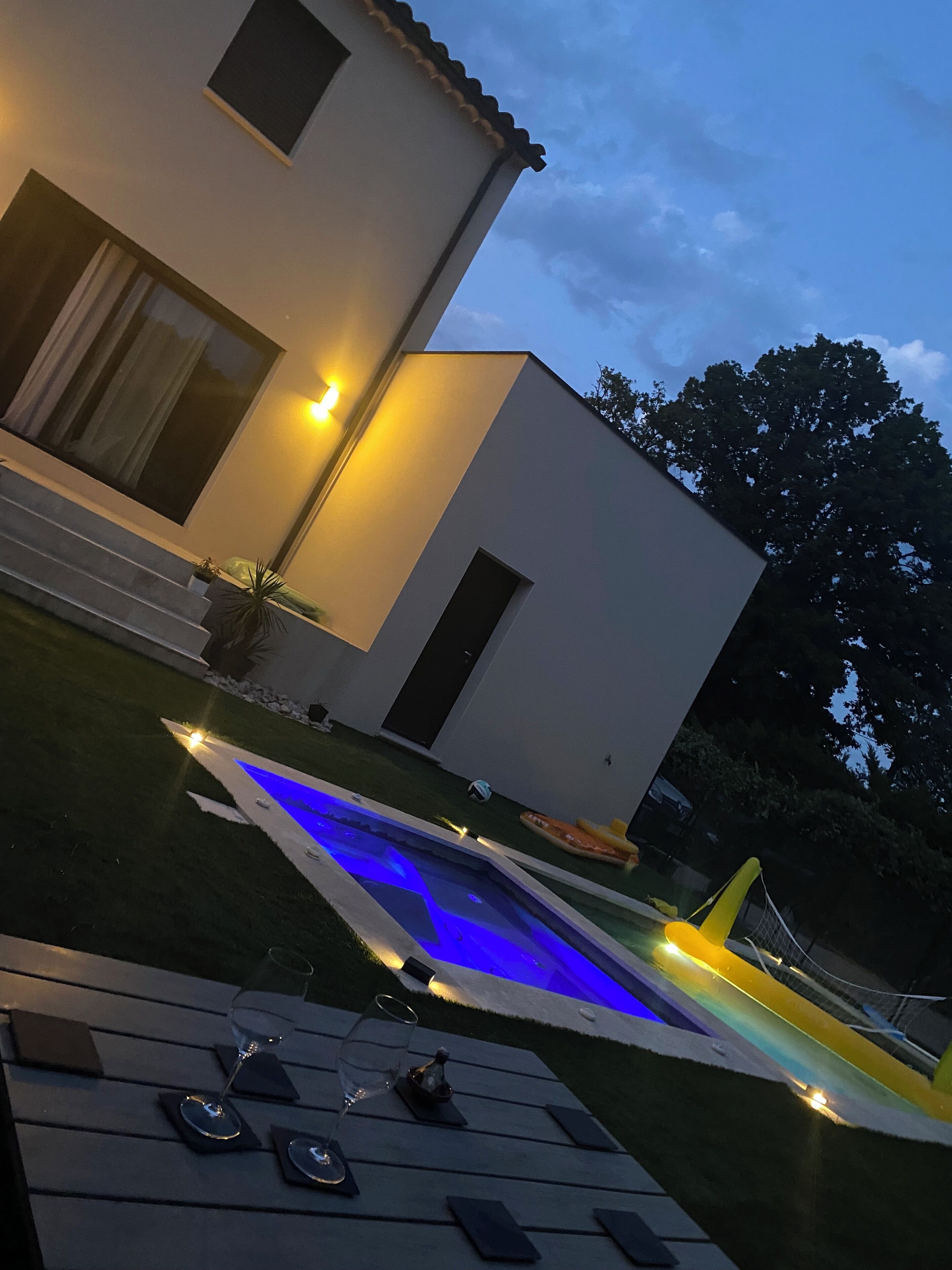 A modern house with a swimming pool, outdoor seating, and a well-lit patio area.