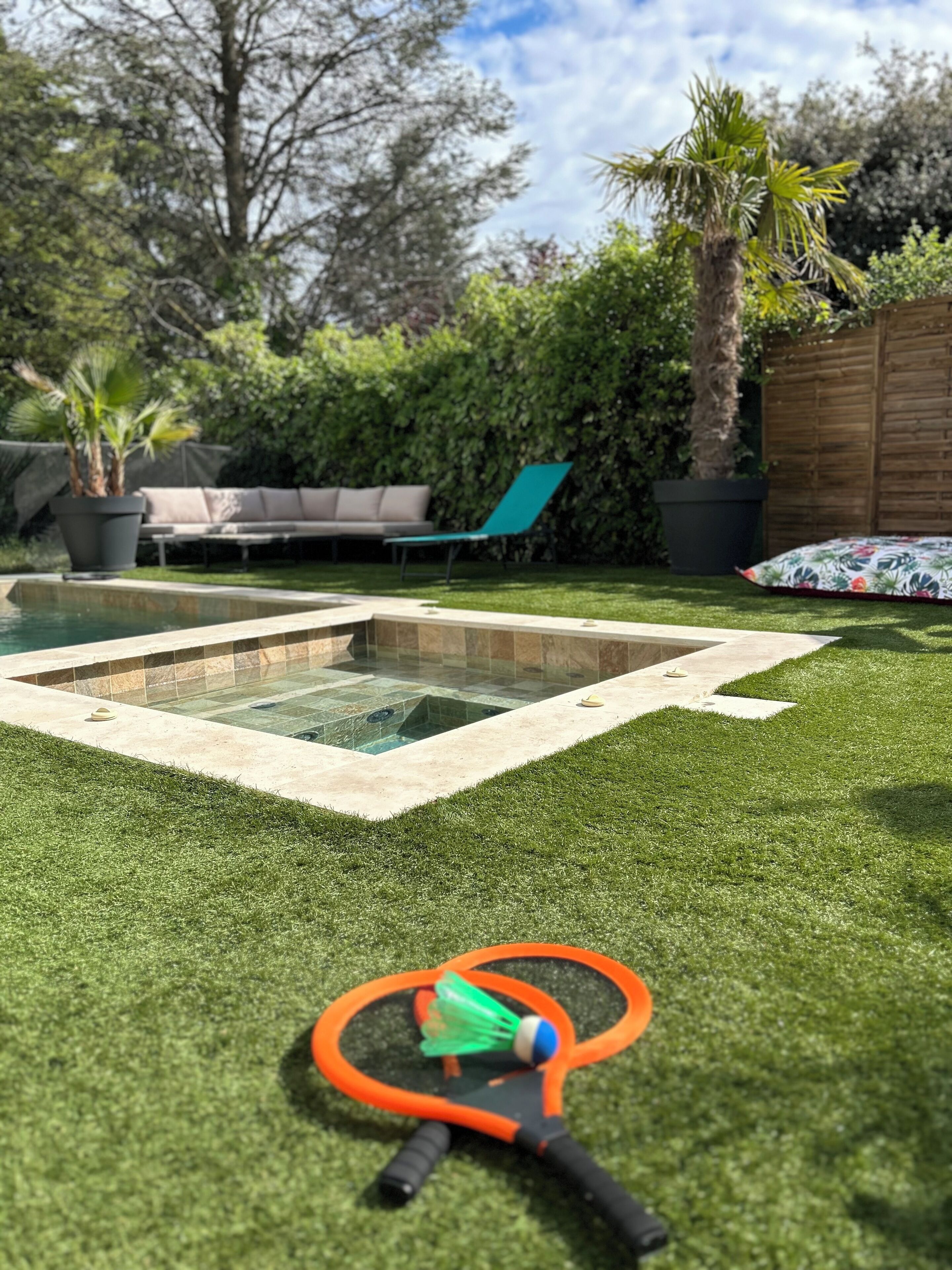 A backyard with a swimming pool, artificial grass, a lounge chair, and a badminton racket.