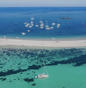 Luchtbeeld van een strand met talloze boten in het water, een zandstrand en helder turquoise water.