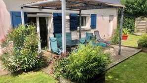 Eine überdachte Terrasse mit Gartenmöbeln, ein Holzdeck und eine Gartenanlage mit Pflanzen und Blumen.