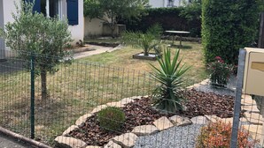 Ein von einer Hecke umgebener Gartenbereich mit unterschiedlichen Pflanzen und einem kleinen Patio-Tisch.