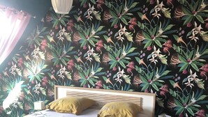 Ein Schlafzimmer mit floraler Tapete, einem hölzernen Bettgestell und einem Nachttisch mit Lampe und Fernbedienung.
