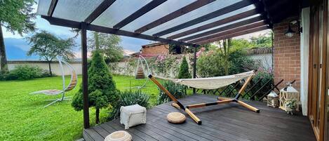 A wooden deck with a hammock, a cushioned bench, and a small table.