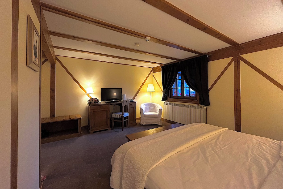 Un dormitorio con una cama, un escritorio con computadora, una silla, un televisor y una ventana con cortinas.