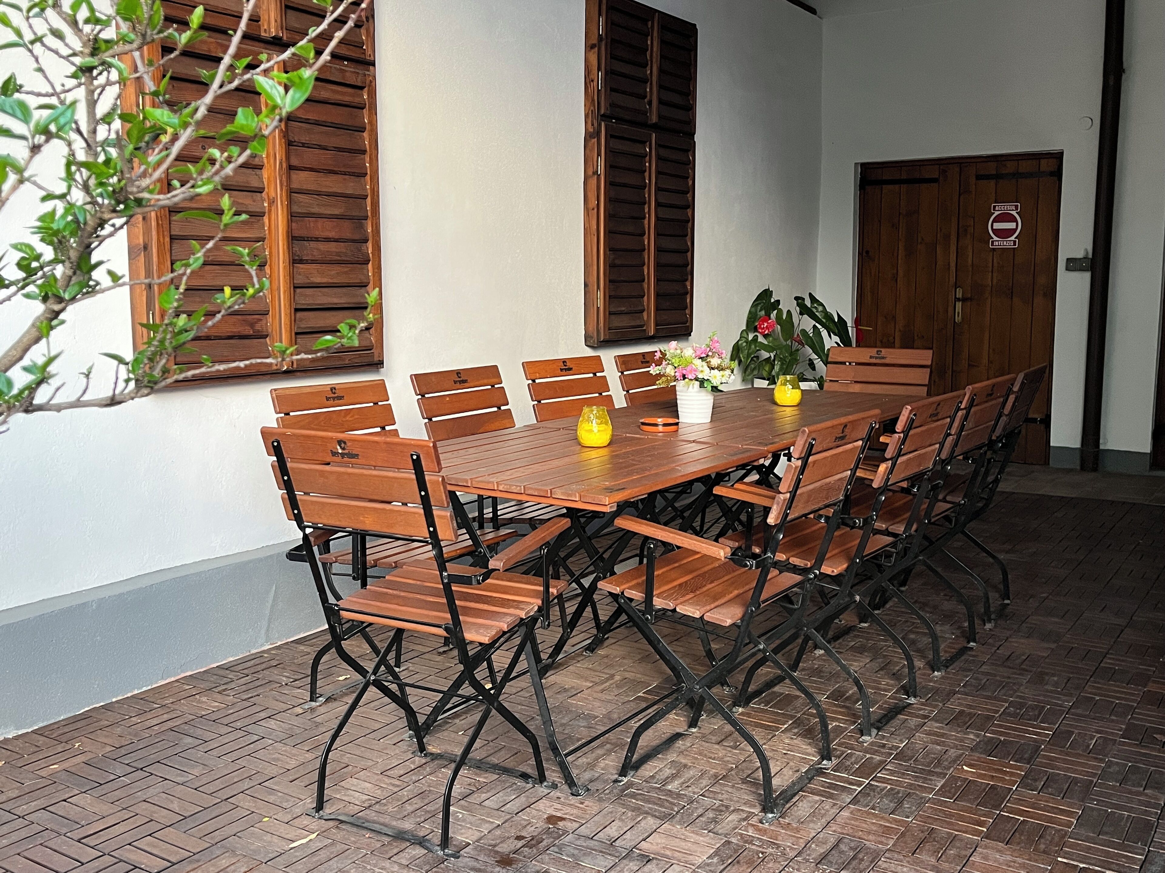 Una mesa de madera con sillas, una planta en maceta y una puerta con un cartel.