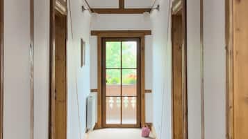 Un couloir étroit avec des poutres en bois au plafond, des murs blancs et une grande porte en bois au fond.