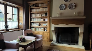 A cozy living room with a fireplace, a bookshelf, and a window with curtains. - Tohanu Vechi (Zarnesti)