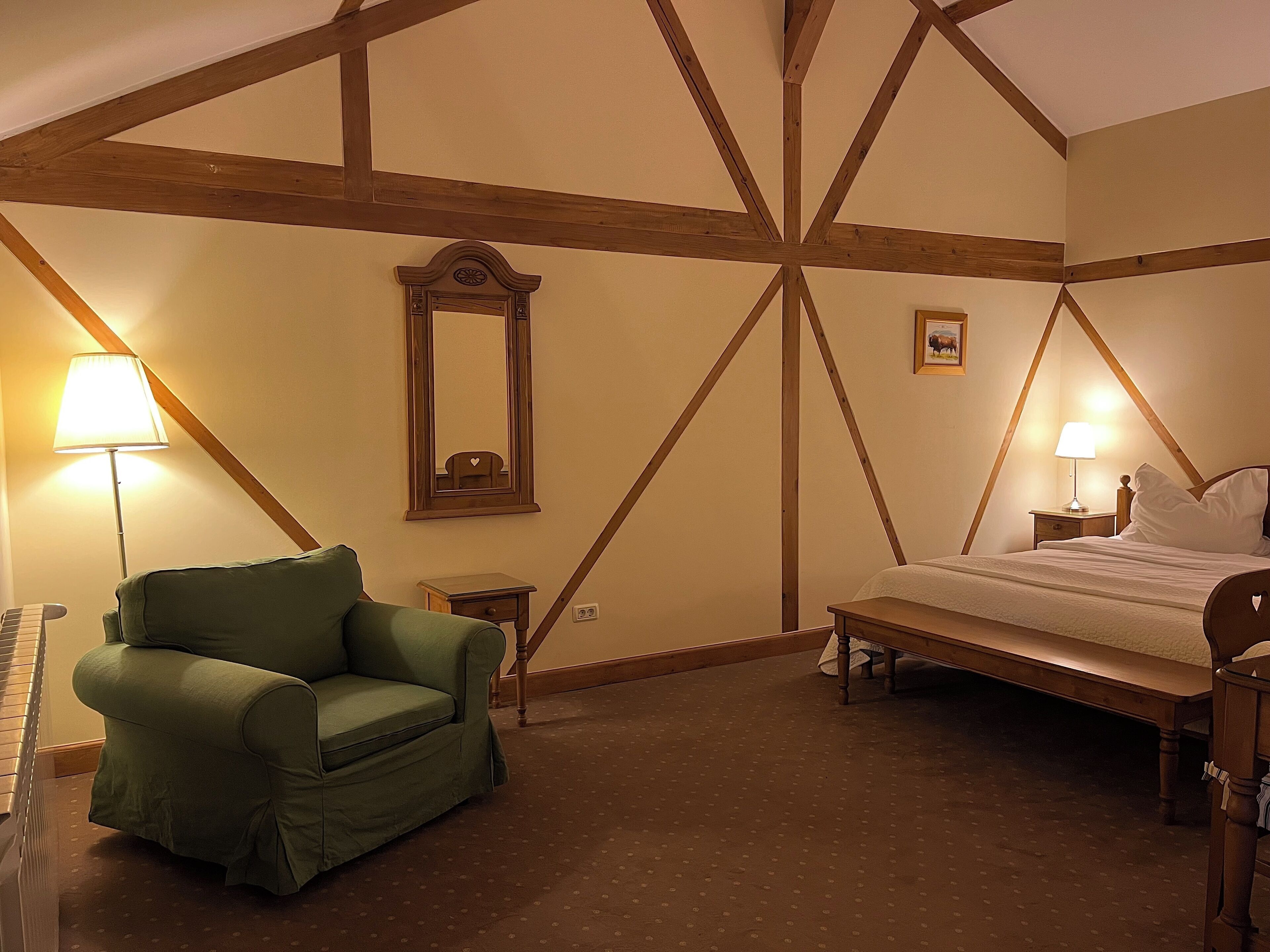 Un dormitorio con cama, un sillón verde, una mesita de noche, una lámpara y un espejo.