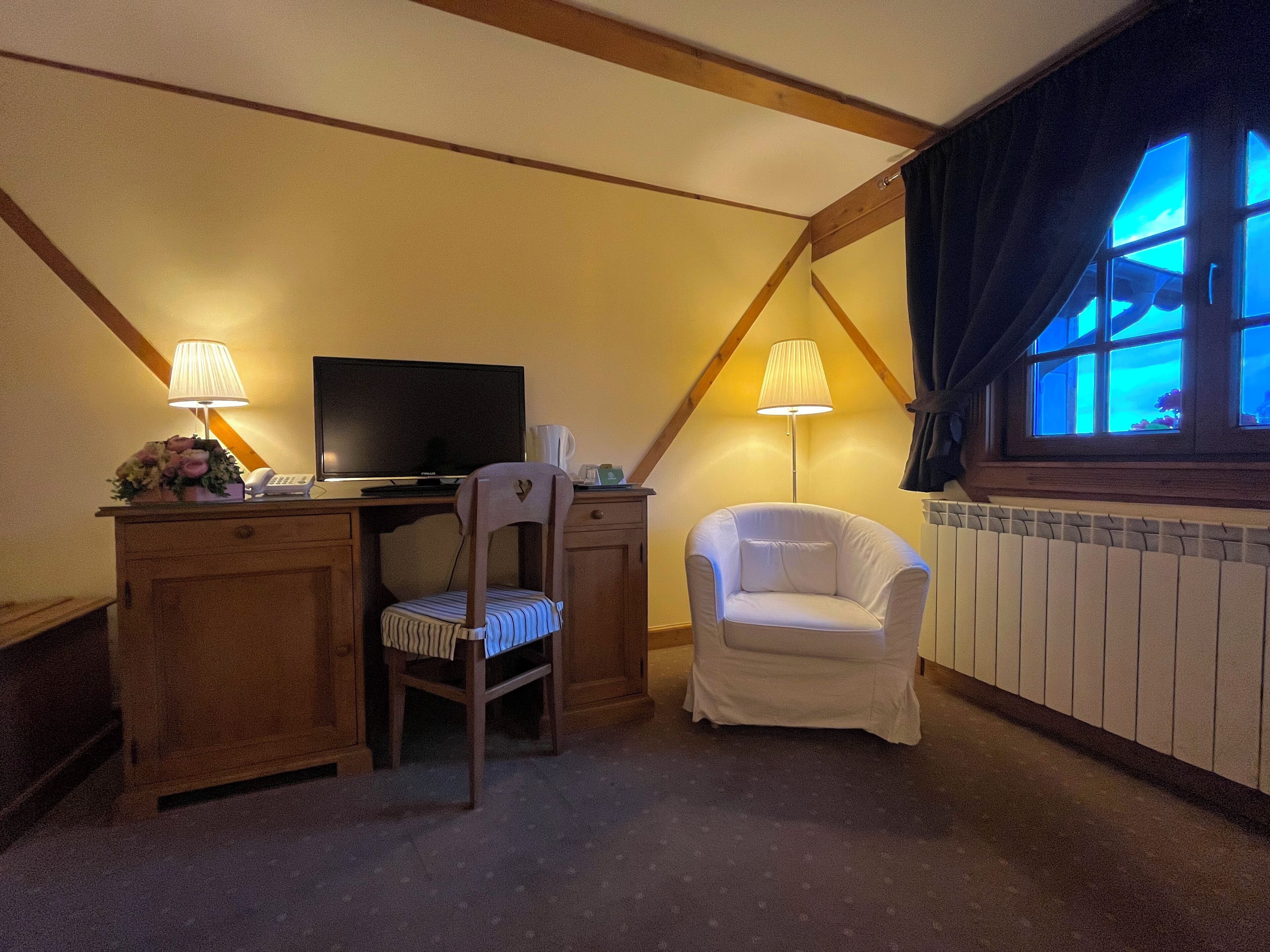 A cozy room with a desk, two chairs, a television, and a window with curtains.
