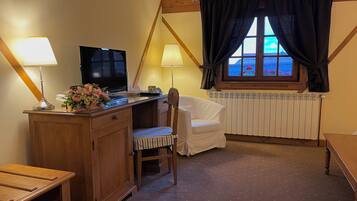 A cozy room with a wooden desk, a chair, a television, and a window with curtains.